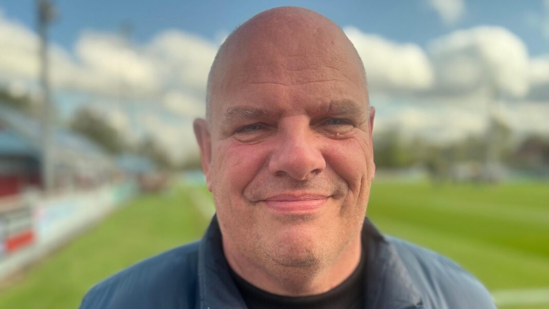 Ex-football chief admits offences linked to woman’s drugging and rape by husband Karl Lindsay, in his 50s, who is bald and clean shaven, stands on a football pitch wearing a blue gilet over a black sweatshirt and smiles at the camera.