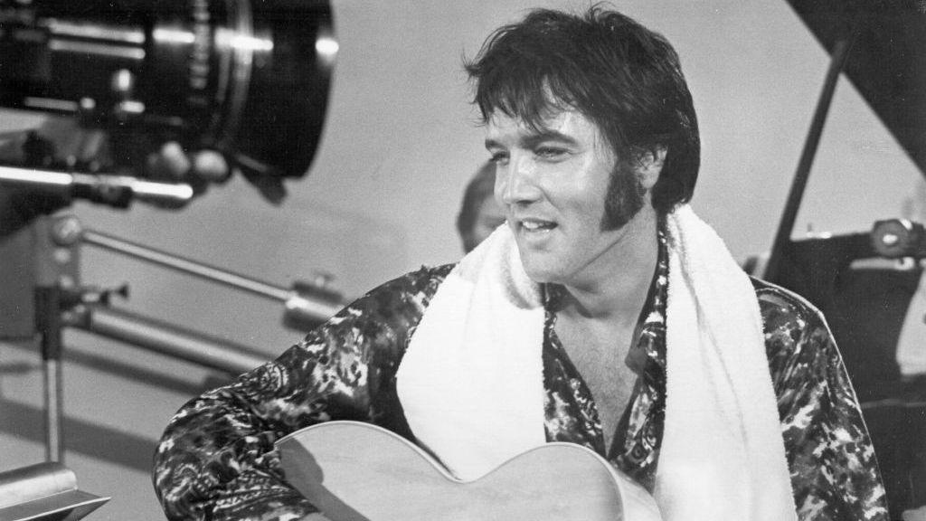 Elvis holding a guitar in a black and white photo from a studio set in 1973