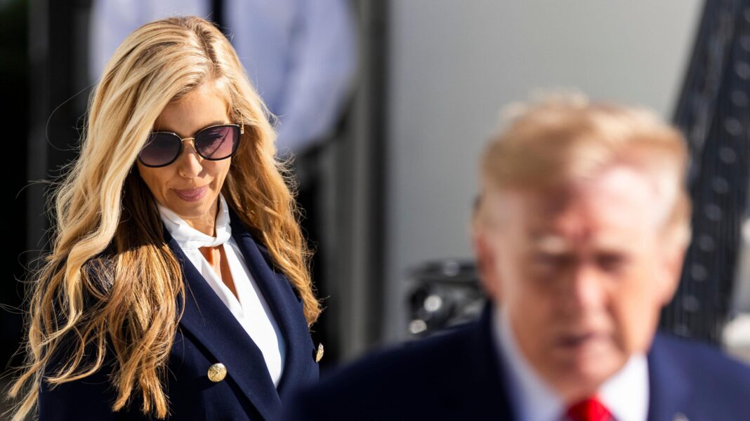 Analysis: Zacharia was thrown into a whirlwind – and failed at a critical time for Trump Katie Zacharia, wearing sunglasses and in a blue suit and white top, looks down. Trump stands in front of her and to the right and is out of focus