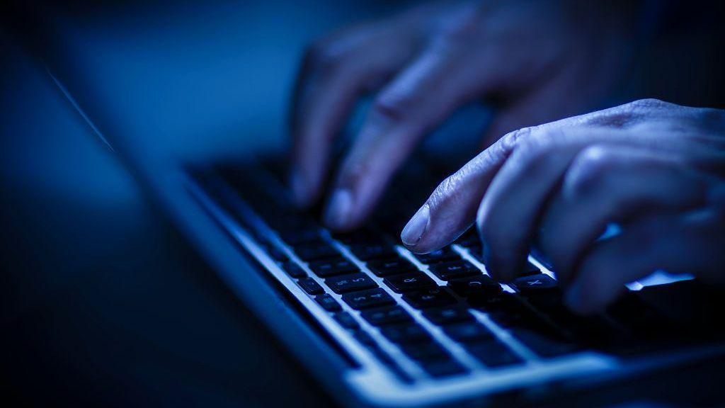 Hands close-up typing on a laptop keyboard in a blue light