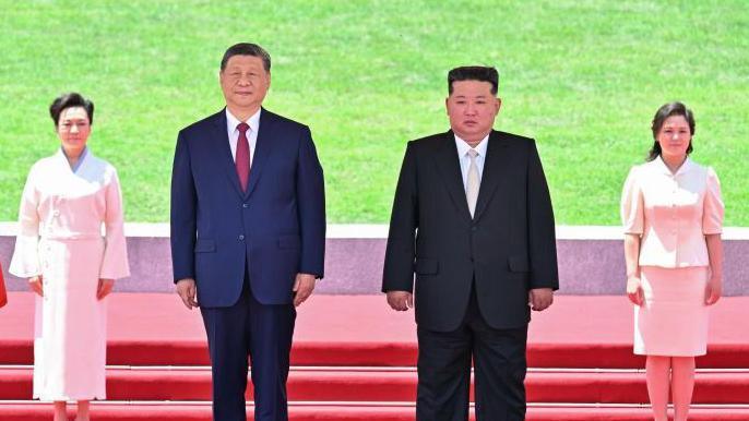 Xi (L) and Kim (R) can be seen here standing on a podium, with their wives behind them
