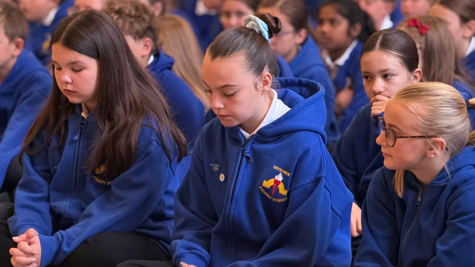 School children are sat down in rows looking at the floor.