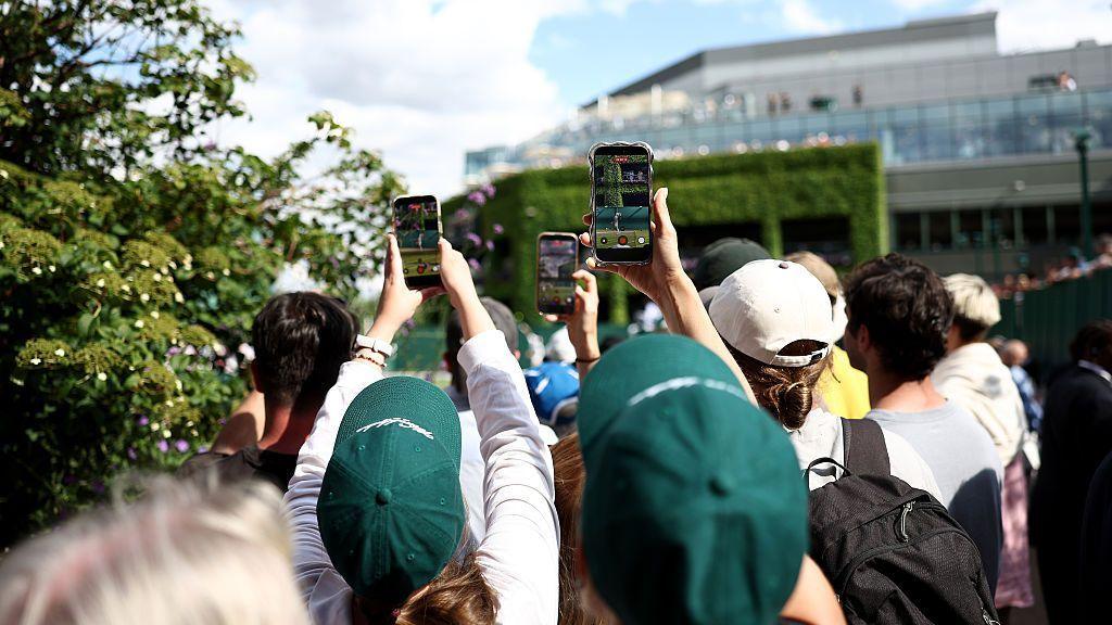 Fans hold up mobile phones outside the show courts at Wimbledon