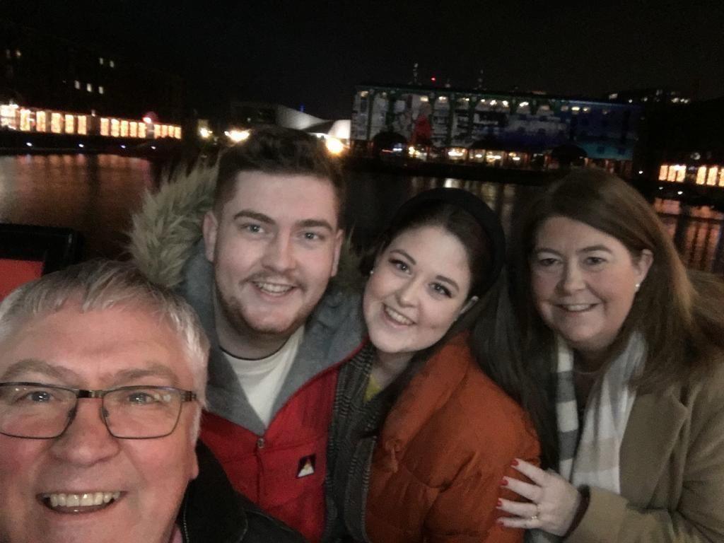 John is taking a selfie in the dark outdoors with James, Amy and Louisa behind him. They are all smiling and wearing coats and scarves