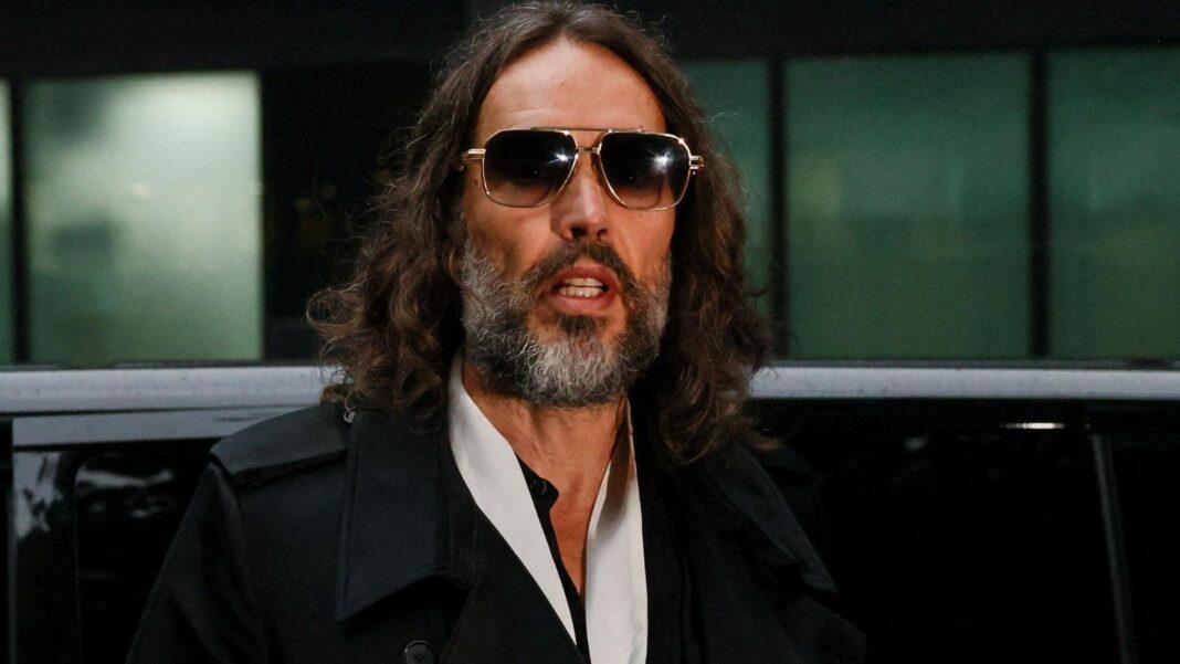 British actor and comedian Russell Brand steps out of a black car at Southwark Crown Court during the second week of his trial on charges of rape and sexual assault involving six women between 1999 and 2009, which he denies. He is wearing sunglasses and a black coat.