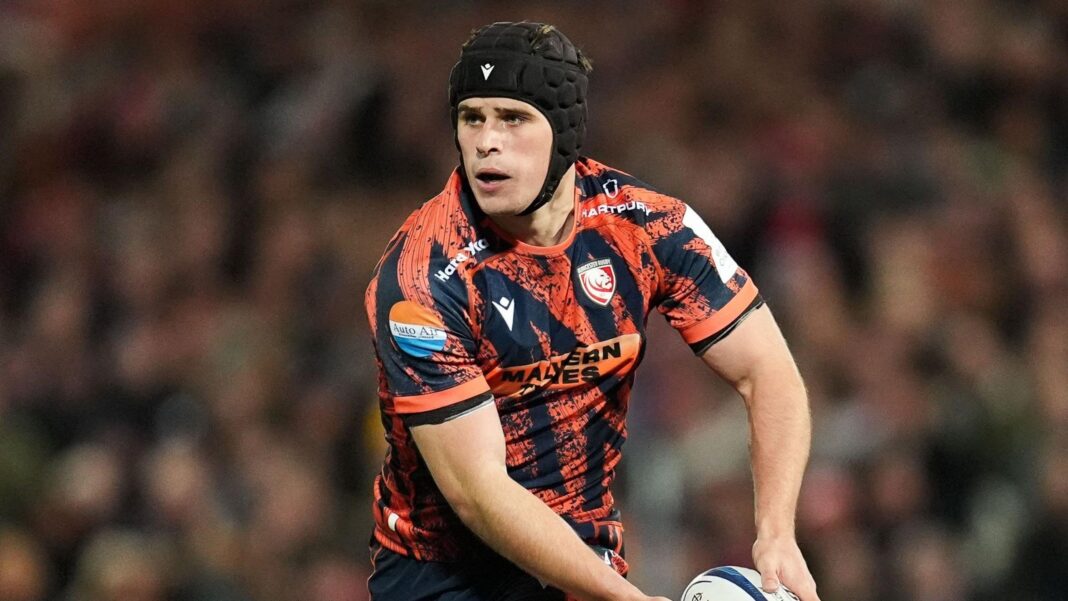 England’s Atkinson stays at Gloucester until 2029 Seb Atkinson holds a rugby ball to his side during a Champions Cup match against Bordeaux. He is wearing a scrum cap and Gloucester rugby 2026-27 European kit.