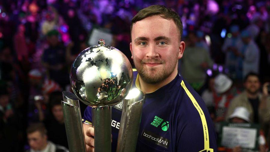 Luke Littler pictured with his first of two PDC World Darts Championship titles.