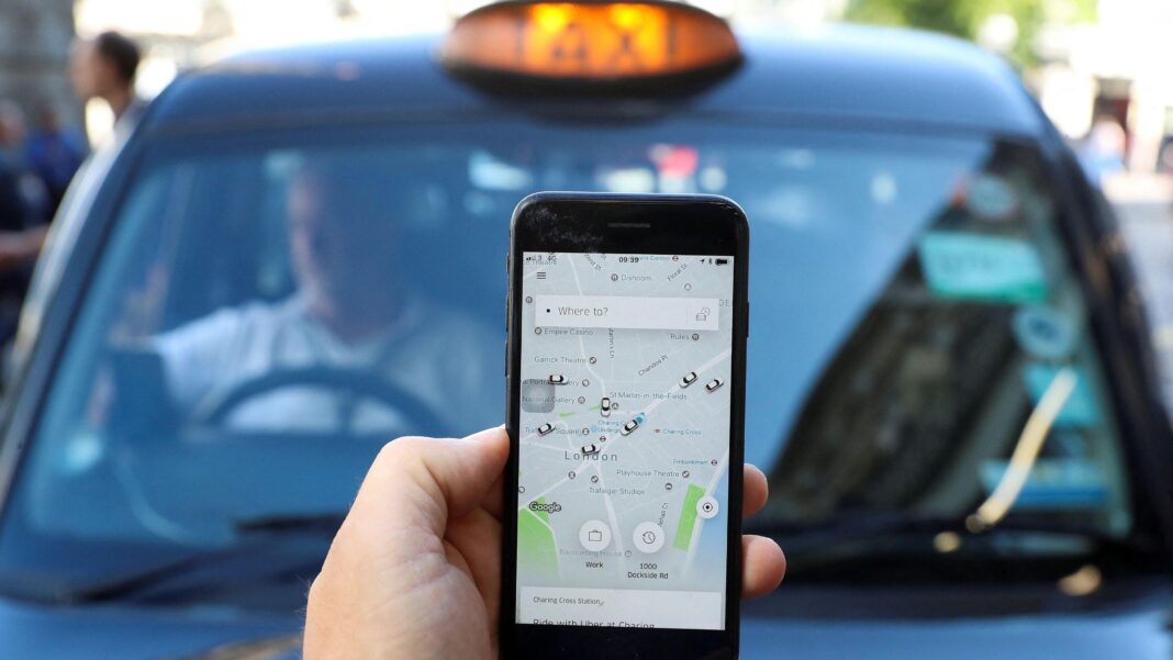 Uber wins bid to throw out £200m black cab claims Phone showing Uber app and a London black cab in the background.