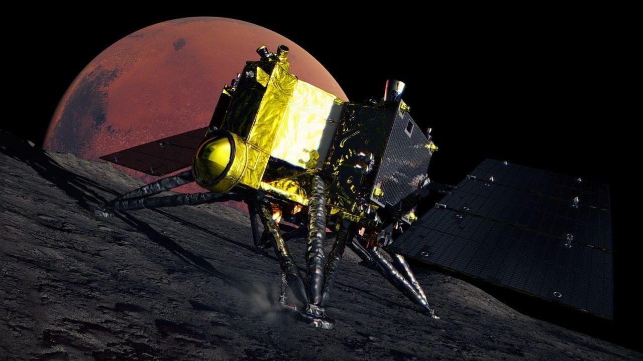 An artist's impression of the MMX  spacecraft on the dark, rocky surface of Phobos. The spacecraft is gold and black and has four triangular legs and dark solar panels. The red disc of Mars is in the background.