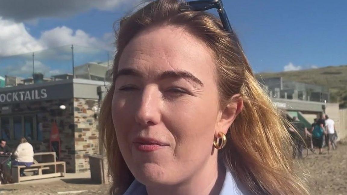 A woman called Jamie-Lee Job. She appears to be squinting. She has shoulder-length brown hair which has blonde highlights in it. Her sunglasses are propped on top of her head. She has make up on.