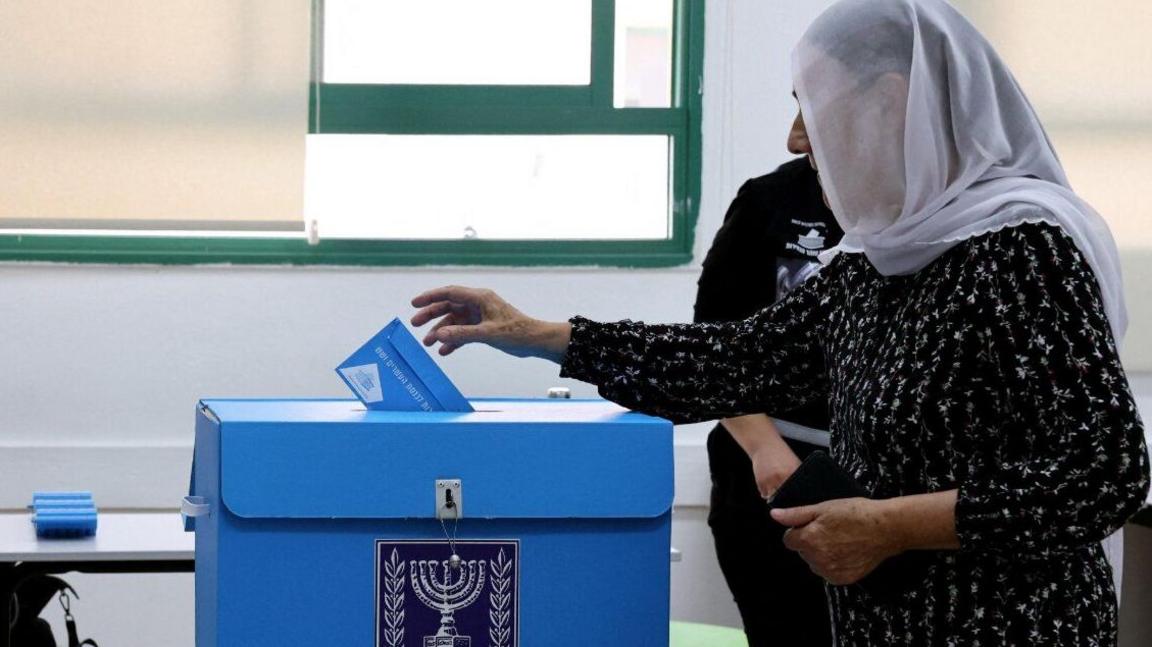 A woman wearing a headscarf puts a ballot paper in a ballot box in Israel's general election (27/1026)/