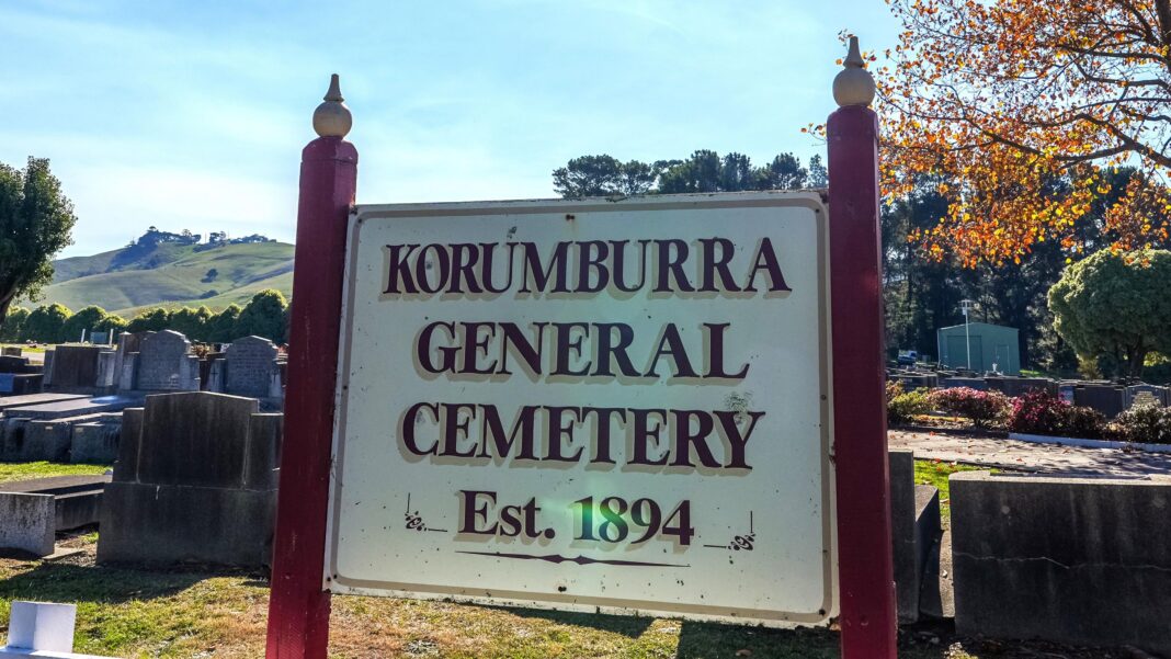 A sign for Korumburra General Cemetery, with headstones and hills in the background