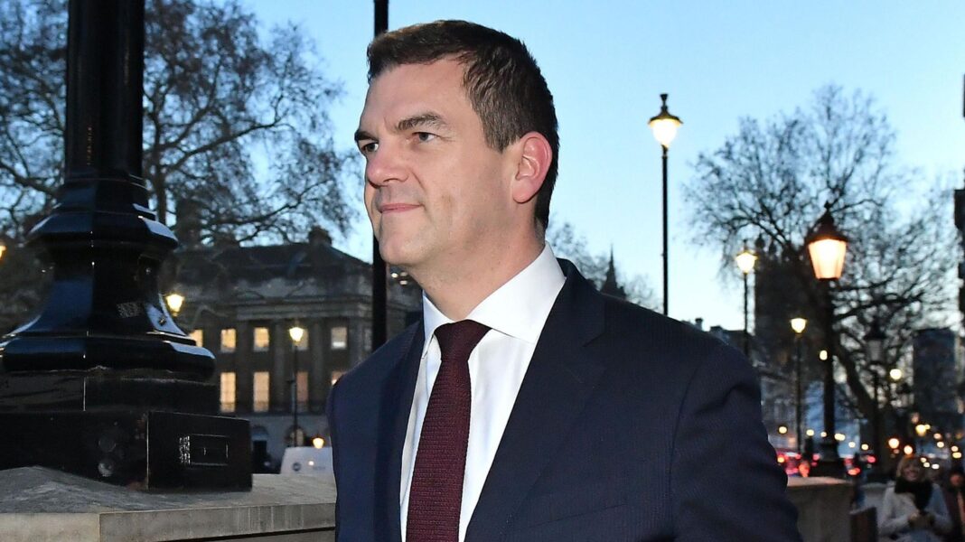 Sir Olly Robbins walking down Whitehall wearing a suit and tie.