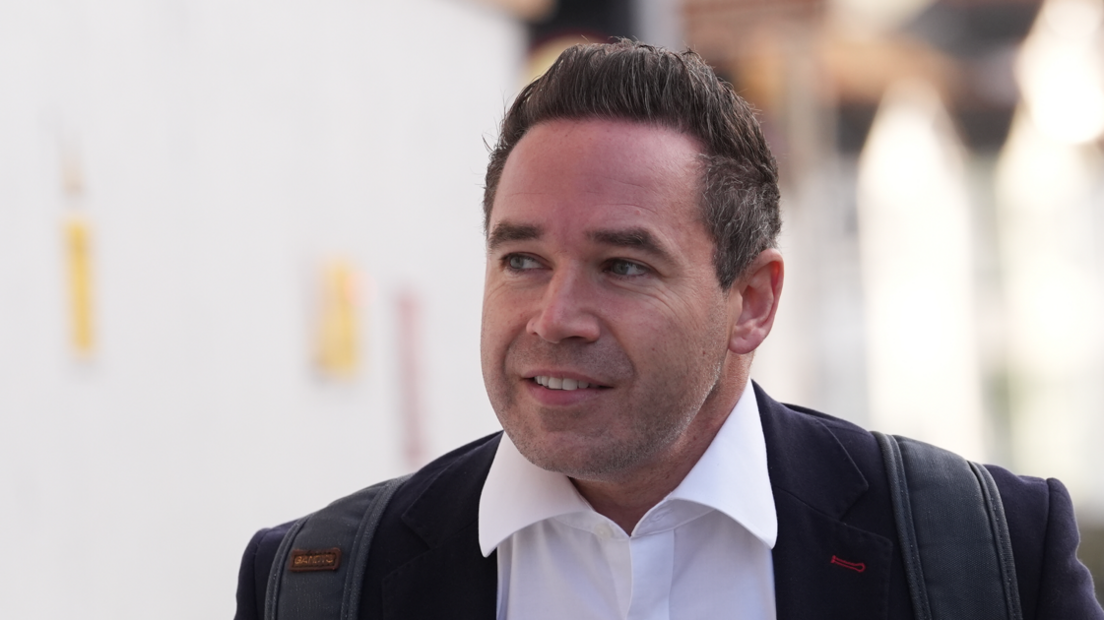 A man with short black hair wearing a suit jacket and white shirt. He is looking away from the camera.