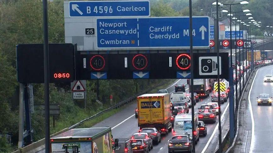 A wide shot of the M4 in Newport shows queues of cars on one side of a three-lane motorway.