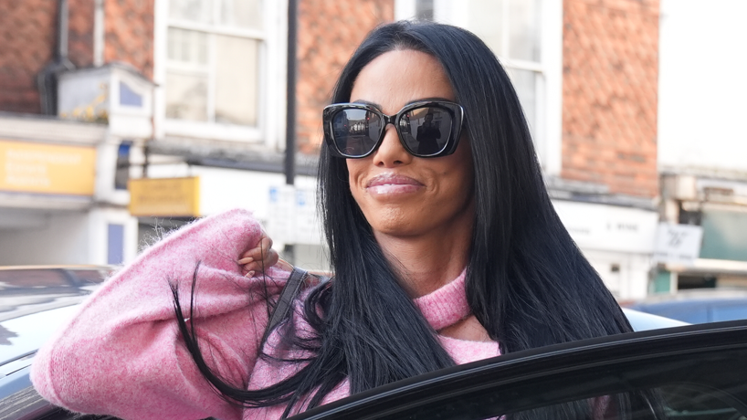 A woman with long black hair, sunglasses and a pink jumper gets out of a car