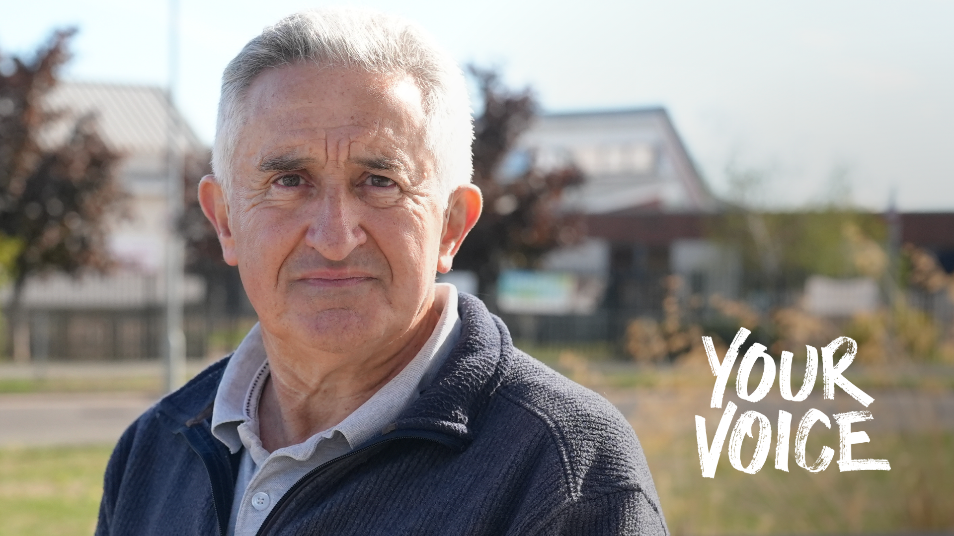 Bryn Dymott, wearing a polo shirt and cardigan, standing on grass in front of some buildings blurred in the background. The words "Your Voice" are imposes on the photo on the left.