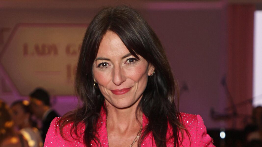 Davina McCall in 2024 is smiling at the camera. She has shoulder-length dark hair and is wearing a sparkly pink jacket.