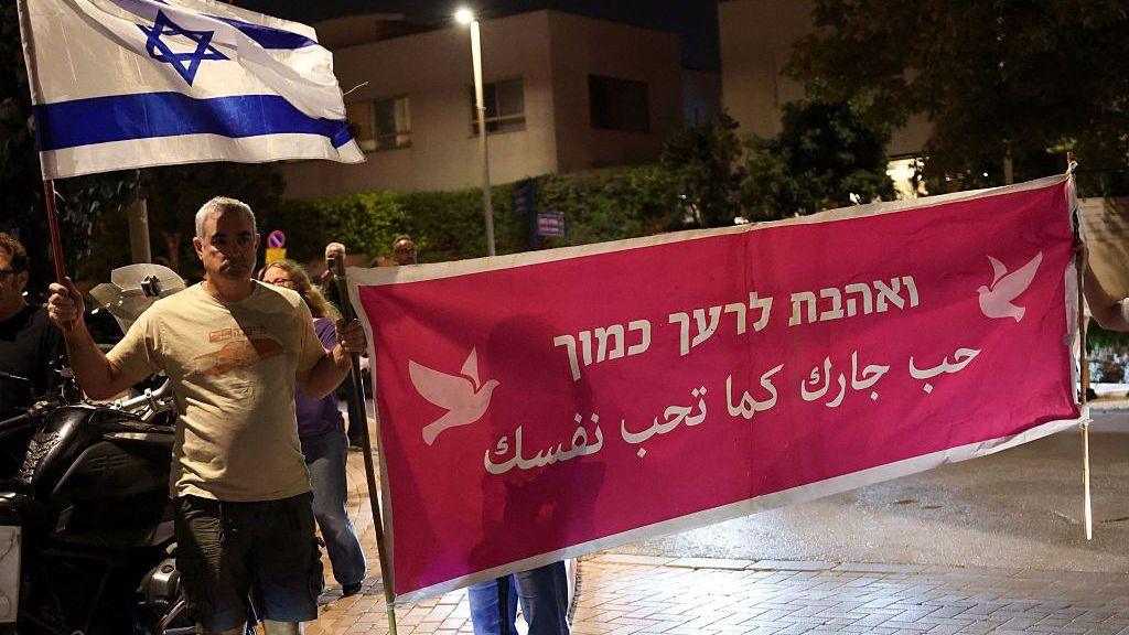 People demonstrate holding a banner that says "Love your neighbour" in Arabic and Hebrew
