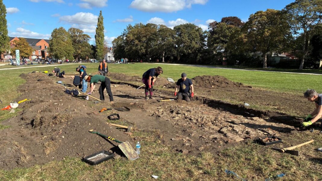 Medieval leprosy hospital uncovered in Lincoln A wide view of the park where a huge pit about a foot deep has been dug. The soil removed from it lies on either side. Various people are bent down looking into the pit.