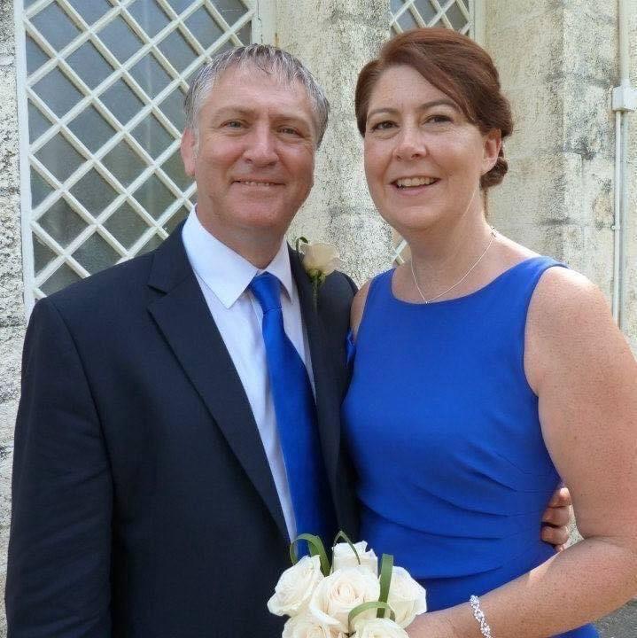 John, in a navy suit and blue tie, and Louisa, in a bright blue dress, at a family wedding