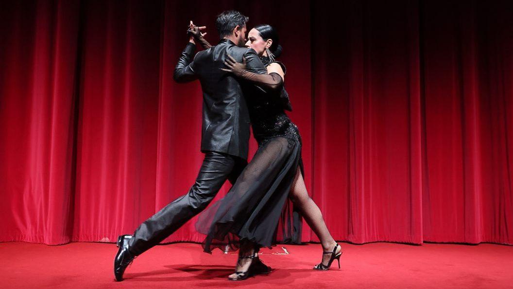 two Latino dancers perform on a curtained stage