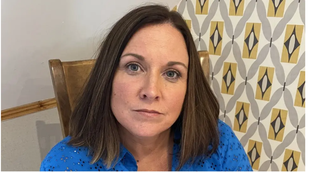 Claire Robinson - a woman with a brown bob and bright blue blouse - looks at the camera with a neutral expression. She is sitting on a wooden chair in front of a patterned wall.