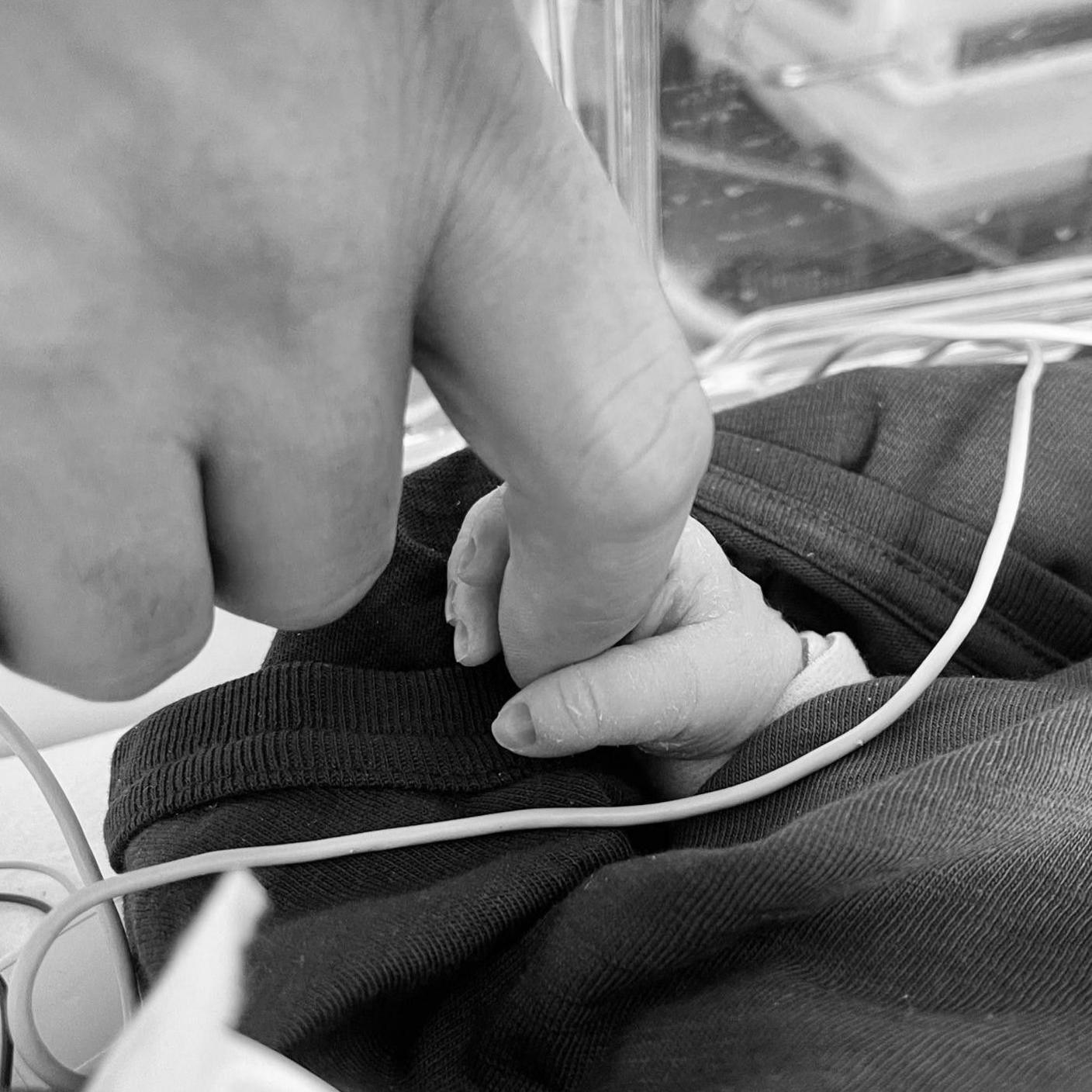 A black and white image of Poppy's tiny hand poking out from a wrap holding onto an adult's finger.