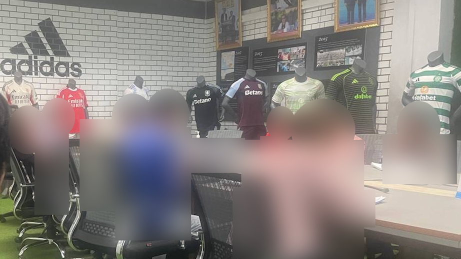 People are sat at a table in a meeting room. Mannequins display Benfica, Aston Villa and Celtic kits beneath an Adidas logo on the wall.
