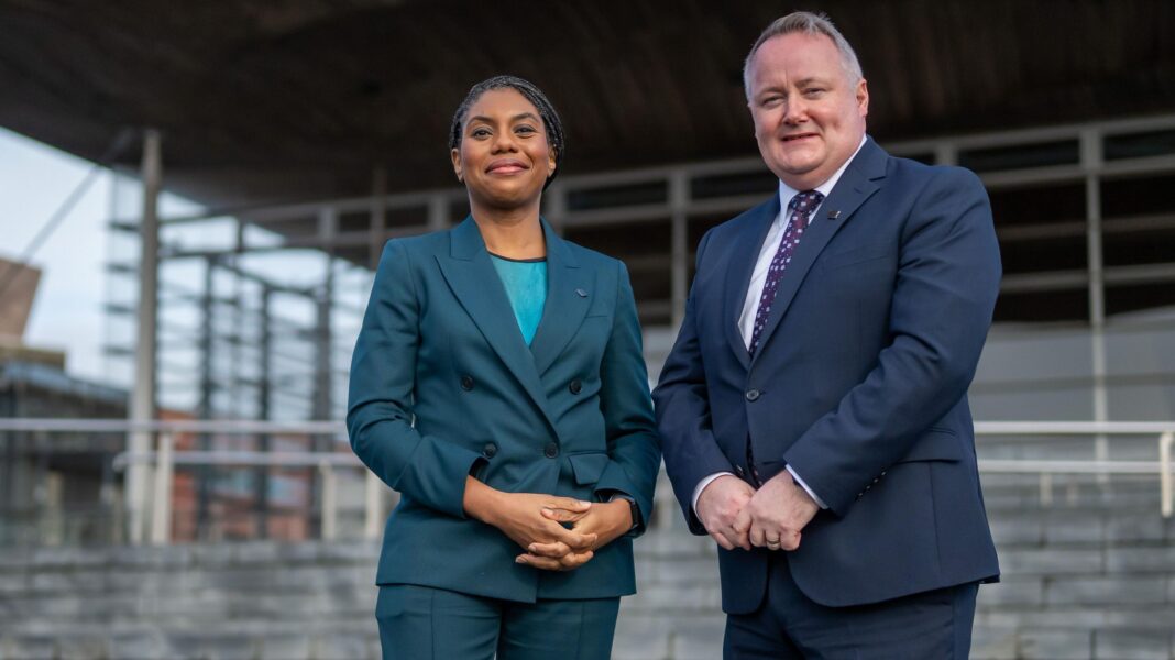 ‘Get on with the day job’ – Welsh Tory leader attacks first minister’s independence push Kemi Badenoch wearing a teal suit stood next to Darren Millar. He is wearing a navy suit with a purple patterned tie.