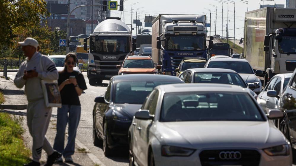 People in Kyiv, Ukraine, walk on the pavement as cars are seen stuck in a huge traffic jam caused by overnight Russian attacks. Photo: 2 October 2026