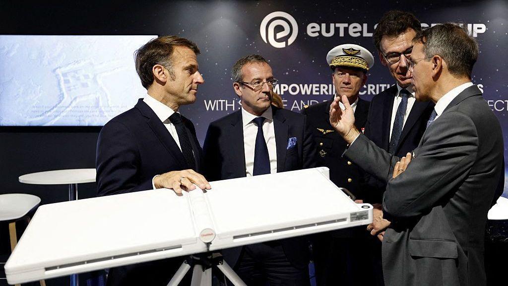Macron and four other men, standing around the terminal talking, at an expo.