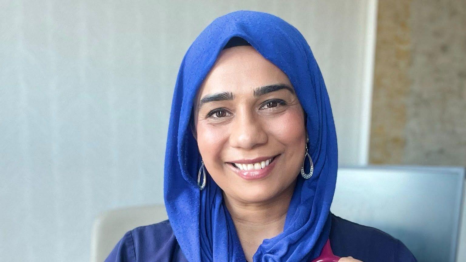 Dr Nighat Arif smiling wearing a blue head dress and hoop earrings