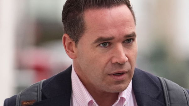 Kieran Hayler- a man wearing a pink shirt and suit jacket walking