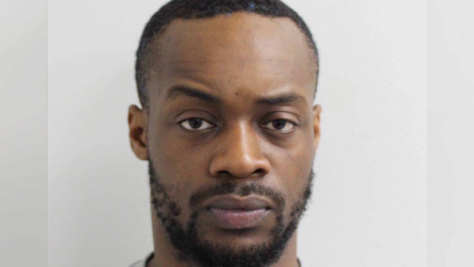 Gogoa Lois Tape, who has a small beard and very short hair, looks at the camera for a police custody photo