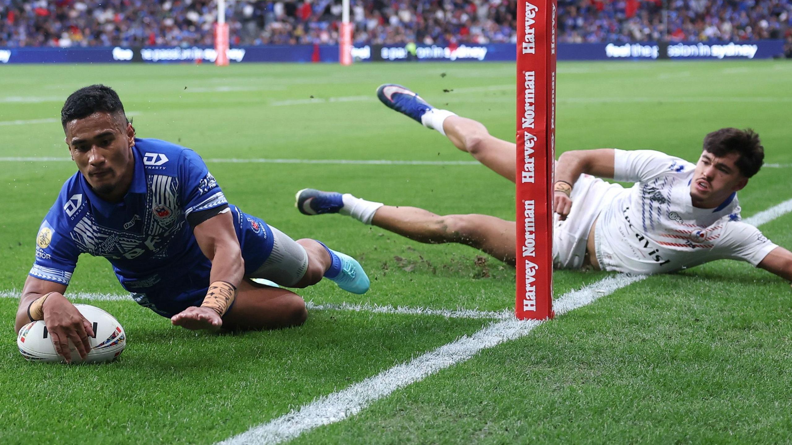 Sua Fa'alogo dives to score a try as a France defender lies on the ground watching him