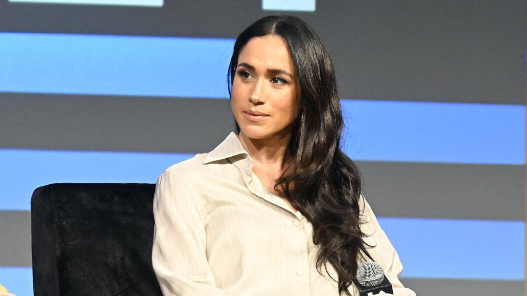 Meghan looks to the left of frame while sat onstage with blue and black background behind her, at SXSW in Austin in 2024.