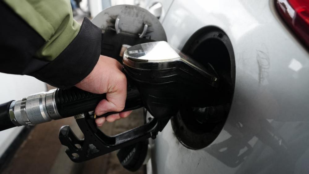 A diesel fuel pump is inserted into a grey car at a petrol station.