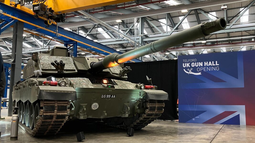 Tank barrel production returns to UK after 20 years A green tank is in the middle of a large warehouse building as part of a display. There is a display board next to it with a union flag background and it says "Telford UK Gun Hall Opening".