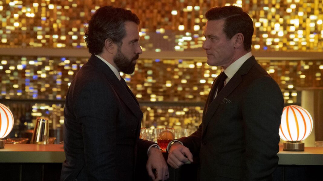 Hollywood actor Luke Evans on ‘joyous’ four months filming in rainy Wales Tom Cullen (left) and Luke Evans (right) are photographed in character as Ben Fitzmaurice and Martin Gilmour. The pair are stood next to a bar in a dimly lit room. They are stood to the side and facing each other. They each have an arm against the bar and there hands are close to touching. They both wear black suits and ties, with white shirts.