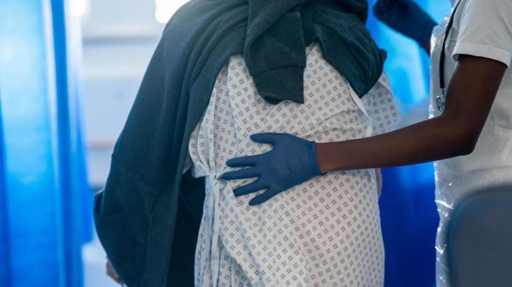 Rear view of a person in a hospital gown being guided by a healthcare professional