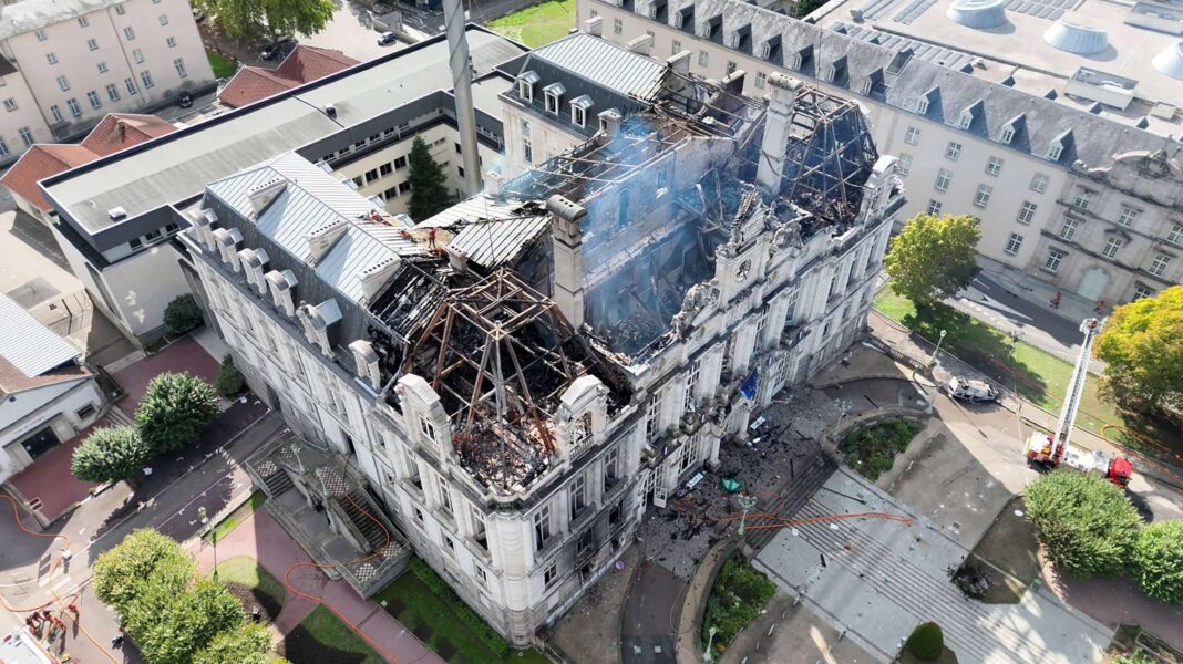 A drone shot shows the burnt roof of the city hall in Limoges. The structure of the top of the building has been revealed by the fire. A fire engine can be seen near the bottom of the building.